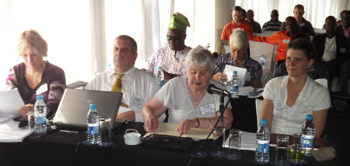 Australian delegates seated at a table. Nigerian delegates and observers are visible in the background.